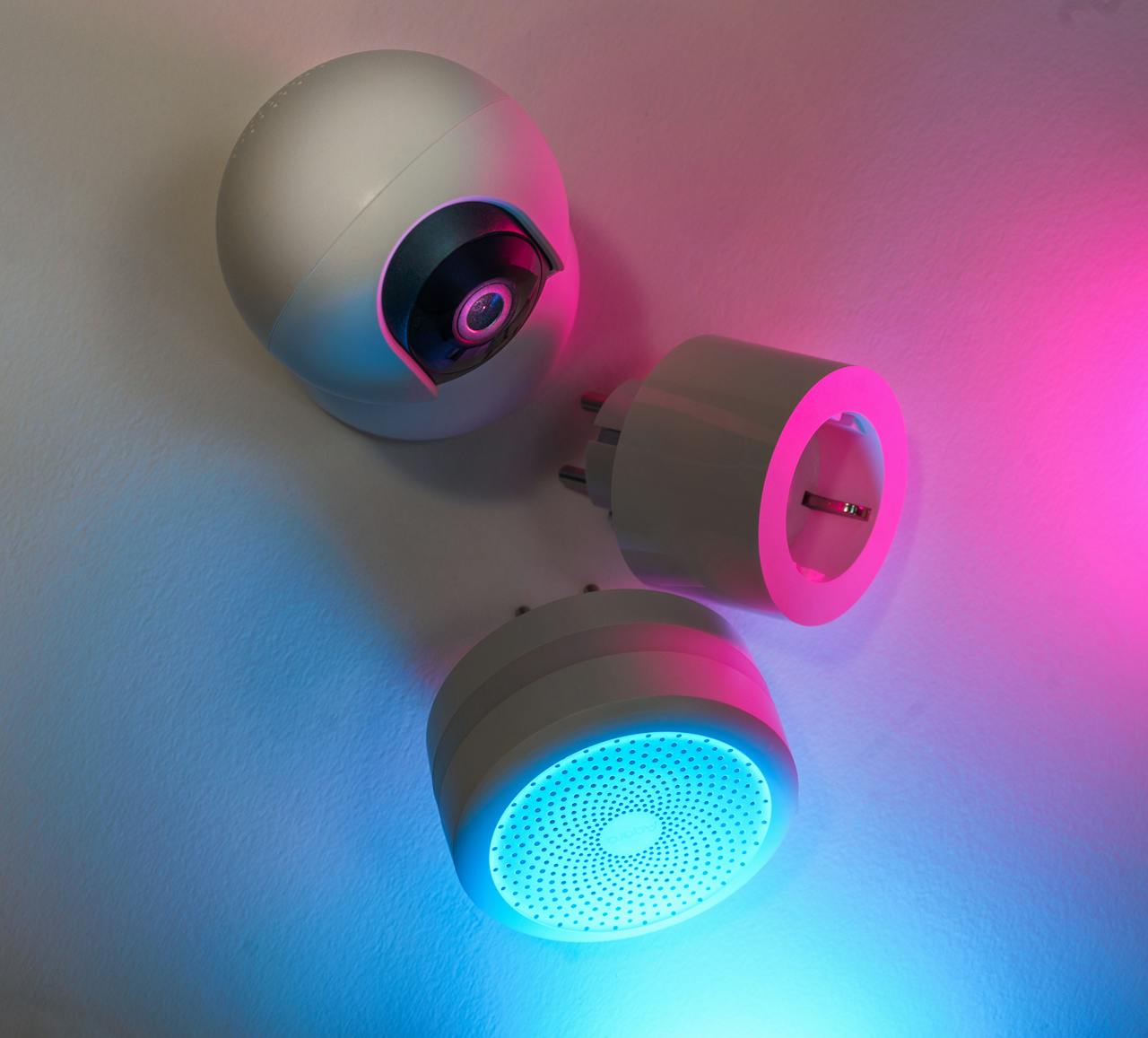 Three smart home devices illuminated by blue and pink neon lights, showcasing technology innovation.