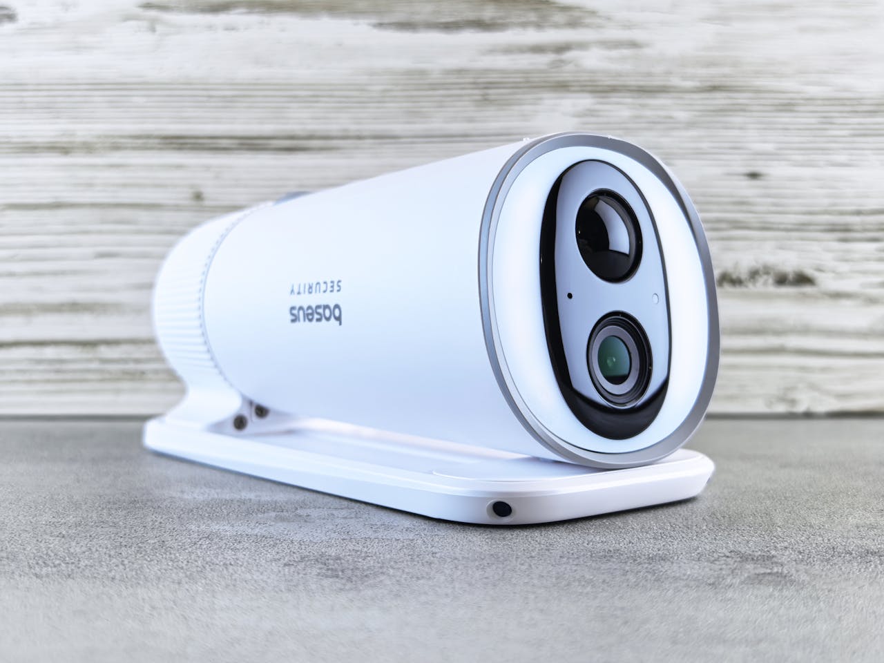 A sleek white security camera with a modern design on a gray surface indoors.